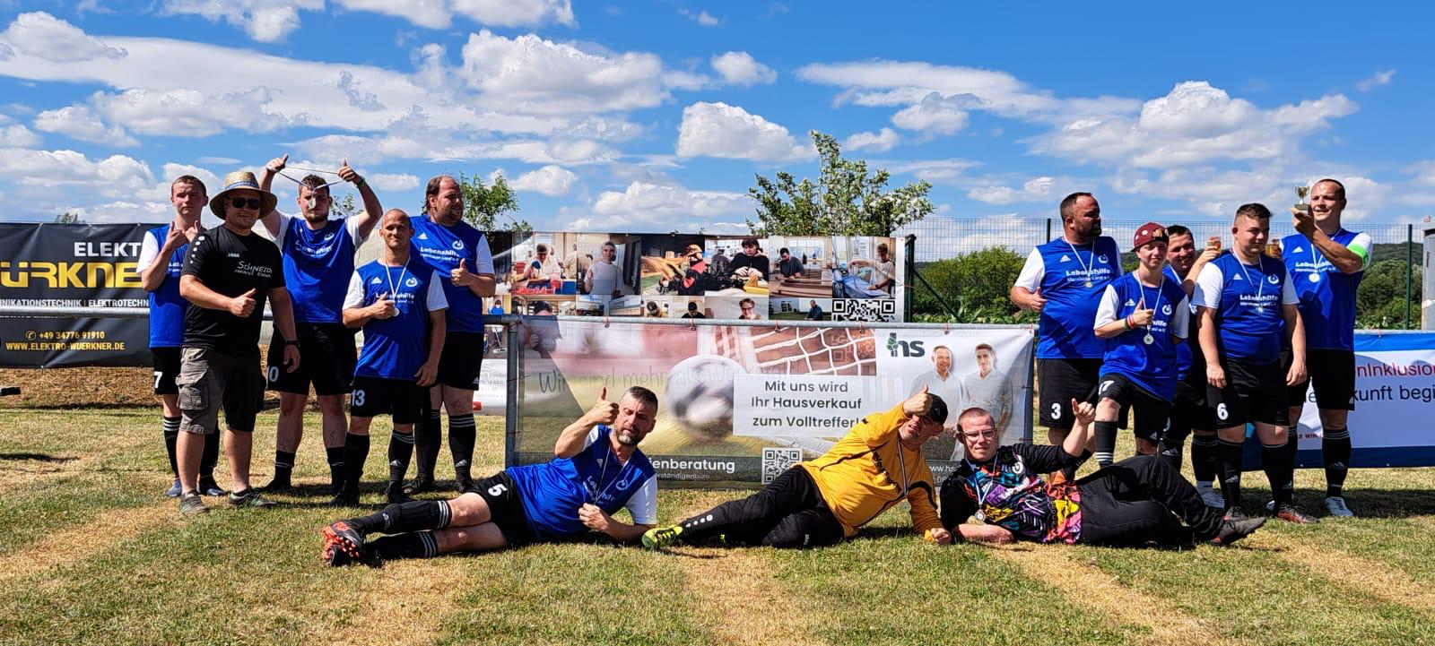 Teilnehmer des inklusiven Fußballturniers der Lebenshilfe Mansfelder Land e.V. vor dem Sponsorenbanner der HS Immobilienberatung in Osterhausen